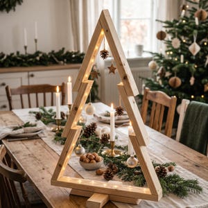 Puede incluir: Un marco de madera triangular con forma de árbol de Navidad, construido con tablones de madera clara. El marco está iluminado por una cadena de luces blancas cálidas y decorado con piñas, estrellas y pequeños adornos colgantes.