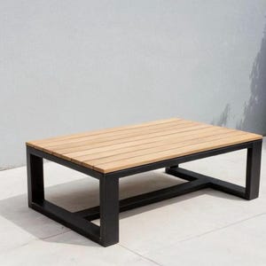Peut inclure: Une table basse en métal noir avec un plateau rectangulaire en bois. La table a un design simple et moderne et est idéale pour une utilisation en extérieur.