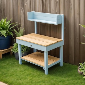 Puede incluir: Un banco de trabajo de madera azul claro con un estante y un cajón. El banco tiene una tapa de madera natural y está sentado en un césped verde.