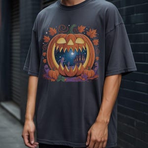 Peut inclure: T-shirt gris foncé avec un motif sur le thème d'Halloween. Le motif comprend une citrouille orange sculptée avec une scène effrayante à l'intérieur, entourée de feuilles d'automne et de petites citrouilles. Le t-shirt est de coupe ample.