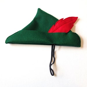 May include: A green felt hat with a red feather and a black string tie. The hat is pointed and has a brim.
