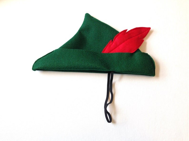 May include: A green felt hat with a red feather and a black string tie. The hat is pointed and has a brim.