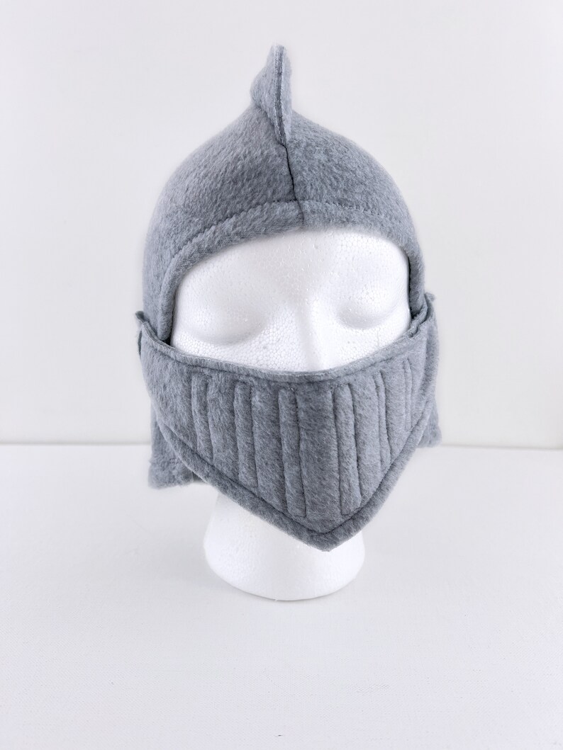 May include: Gray fleece knight helmet with a pointed top and a face mask. The helmet is on a white mannequin head.