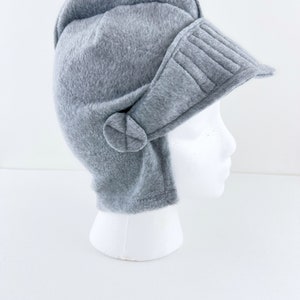 May include: A gray fleece helmet hat with a visor and ear flaps. The hat is on a white mannequin head.
