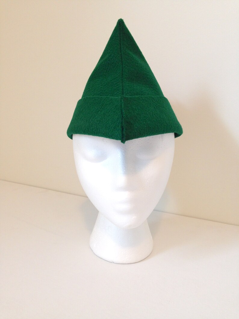May include: A green felt elf hat with a pointed tip. The hat is on a white mannequin head.