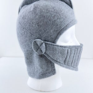 May include: Gray fleece knight helmet with a chin strap and a visor. The helmet is on a white mannequin head.
