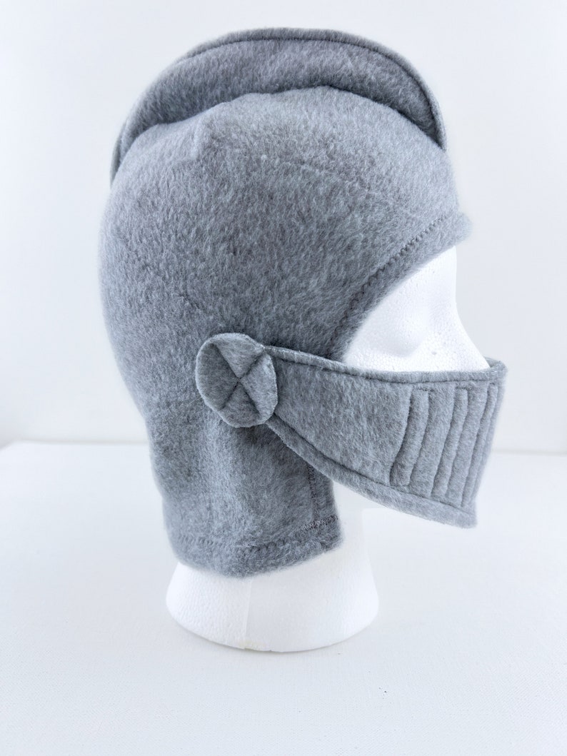 May include: Gray fleece knight helmet with a chin strap and a visor. The helmet is on a white mannequin head.