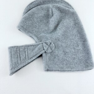 May include: Gray fleece helmet with a flap over the face and a strap that fastens with a button.