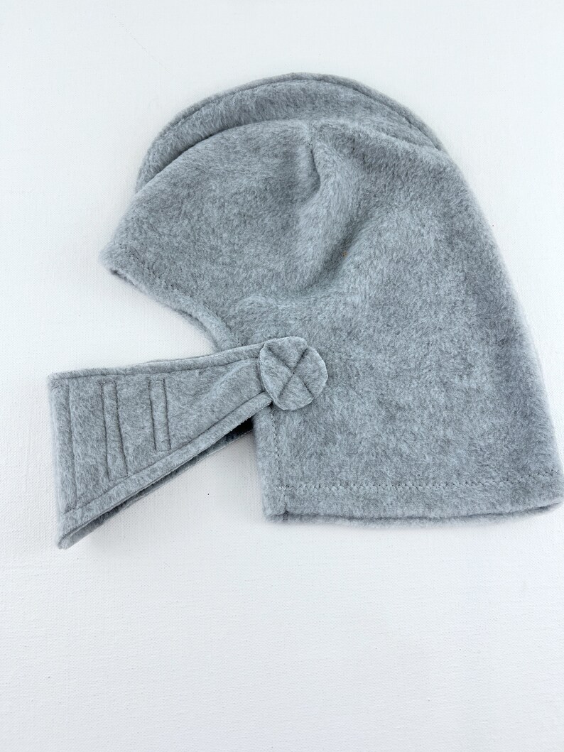 May include: Gray fleece helmet with a flap over the face and a strap that fastens with a button.