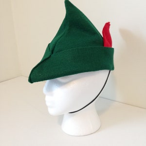 May include: A green felt hat with a pointed tip and a red feather. The hat has a black elastic band.