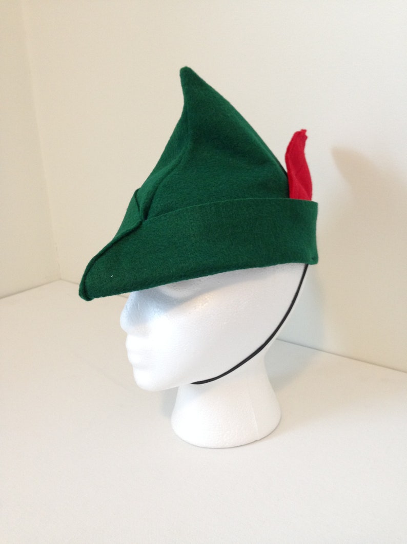 May include: A green felt hat with a pointed tip and a red feather. The hat has a black elastic band.