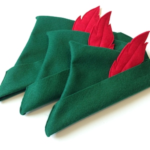 May include: Three green felt hats with red felt feathers. The hats are folded and stacked on top of each other.