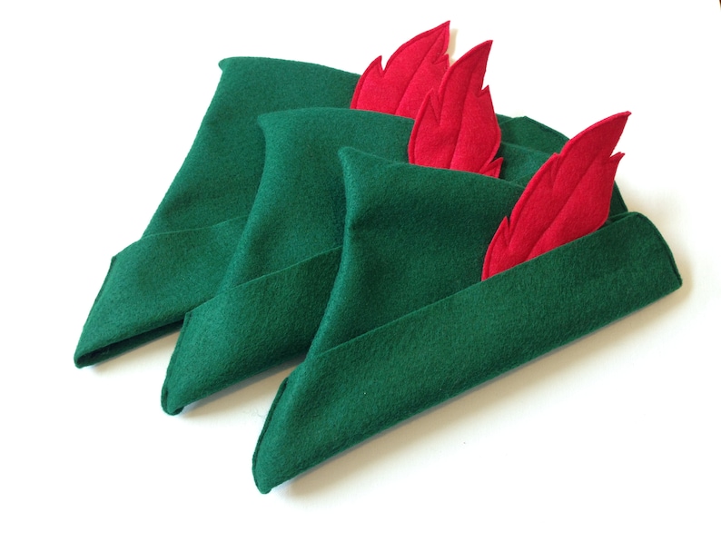 May include: Three green felt hats with red felt feathers. The hats are folded and stacked on top of each other.