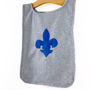 May include: A gray fleece cape with a blue embroidered fleur-de-lis design.