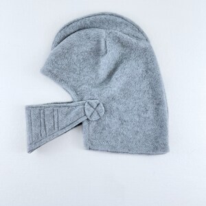 May include: A gray fleece helmet with a visor and a button on the side.