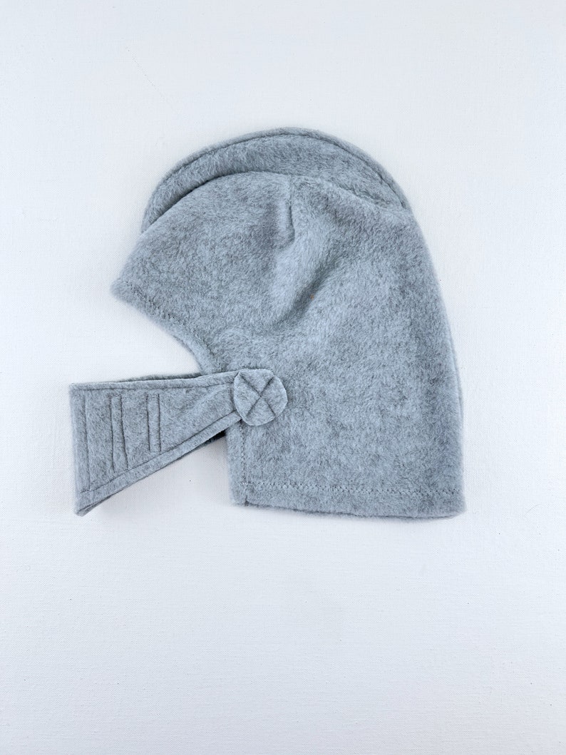 May include: A gray fleece helmet with a visor and a button on the side.