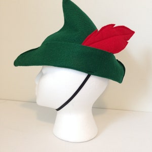 May include: A green felt hat with a pointed crown and a red felt feather. The hat has a black elastic band.
