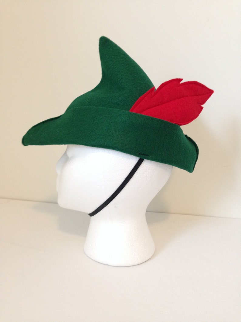 May include: A green felt hat with a pointed crown and a red felt feather. The hat has a black elastic band.