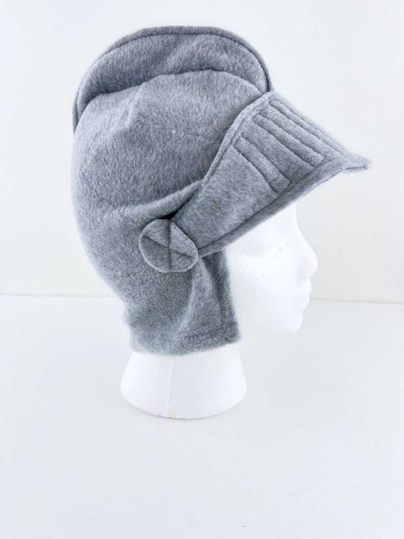 May include: A gray fleece helmet hat with a visor and ear flaps. The hat is on a white mannequin head.