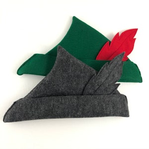 May include: Two felt hats with feathers. The top hat is green with a red feather. The bottom hat is gray with a black feather.