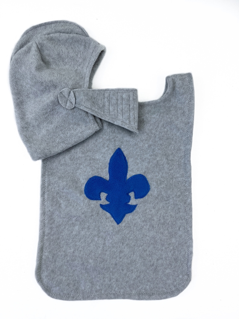 May include: Gray fleece knight costume with a blue fleur-de-lis emblem and a matching hat.