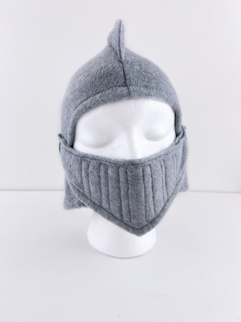 May include: Gray fleece knight helmet with a pointed top and a face mask. The helmet is on a white mannequin head.