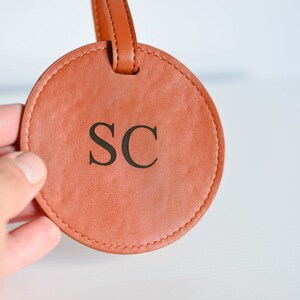 May include: A round, brown leather luggage tag with the initials "SC" embossed in black.