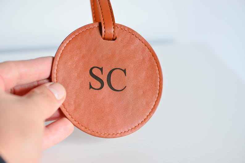 May include: A round, brown leather luggage tag with the initials "SC" embossed in black.