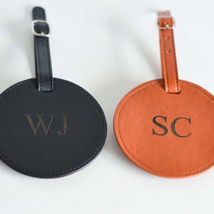 May include: Two round leather luggage tags with black and brown straps. The black tag has the initials "WJ" embossed in gold. The brown tag has the initials "SC" embossed in gold.