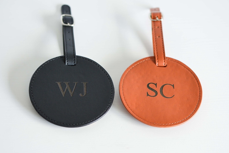May include: Two round leather luggage tags with black and brown straps. The black tag has the initials "WJ" embossed in gold. The brown tag has the initials "SC" embossed in gold.