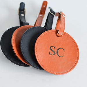 May include: Four leather luggage tags, three are black and one is orange. The orange tag has the initials "SC" embossed on it.