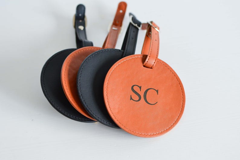May include: Four leather luggage tags, three are black and one is orange. The orange tag has the initials "SC" embossed on it.