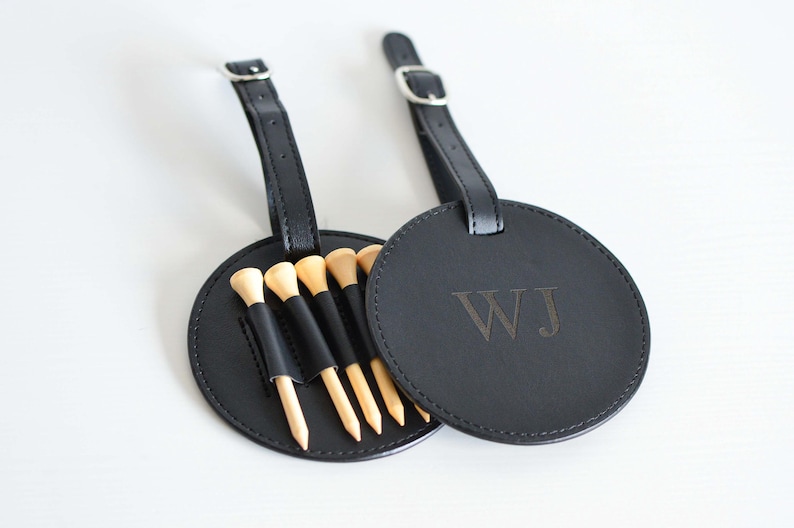 May include: Black leather golf ball holder with a loop for attaching to a bag. The holder has five wooden golf tees and is personalized with the initials "WJ".