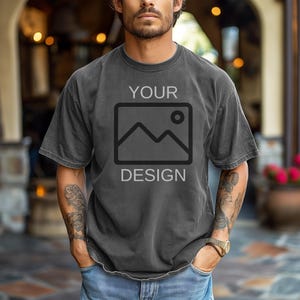 May include: Dark gray t-shirt with the words "YOUR DESIGN" printed on the front. The design features a mountain and sun graphic inside a square. The shirt is worn by a person.