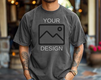 May include: Dark gray t-shirt with the words "YOUR DESIGN" printed on the front. The design features a mountain and sun graphic inside a square. The shirt is worn by a person.