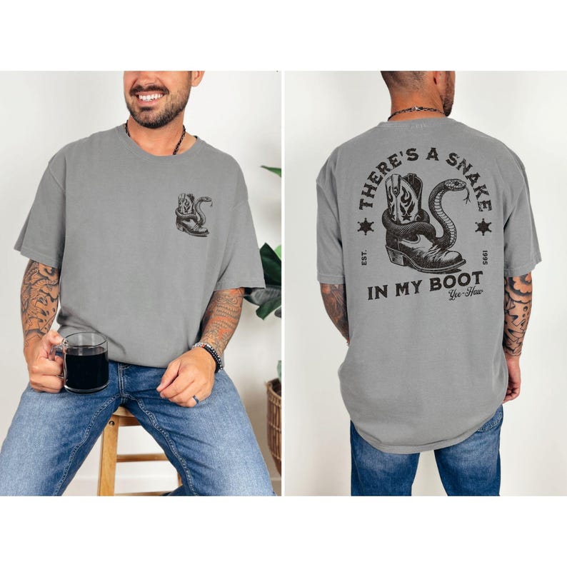 May include: Gray t-shirt with a graphic of a cowboy boot and snake. The back of the shirt features the text "THERE'S A SNAKE IN MY BOOT" in a circular design. The shirt has a relaxed fit.