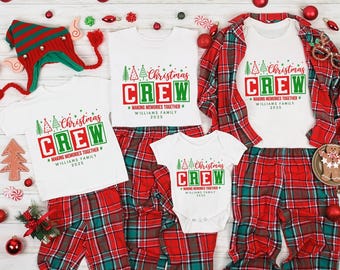 May include: A family Christmas pajama set with white t-shirts printed with "Christmas CREW" and matching red plaid trousers. The set includes a baby onesie, adult shirts, and a plaid jacket. Christmas decorations and a hat are scattered around.