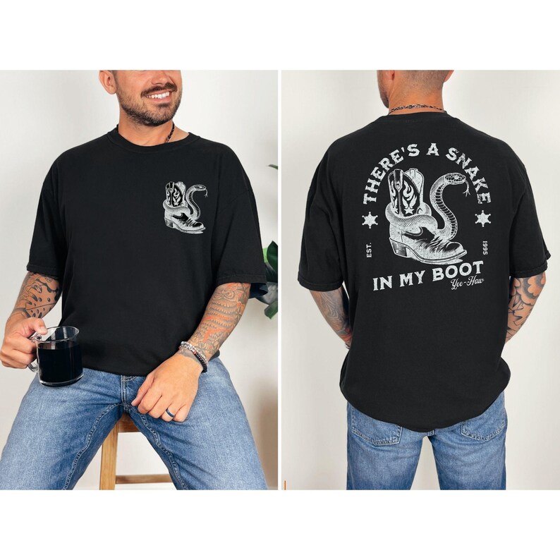 May include: Black t-shirt with a graphic of a cowboy boot and snake. The front of the shirt has a small graphic on the left chest. The back of the shirt has a larger graphic with the text "THERE'S A SNAKE IN MY BOOT".