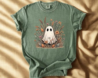 May include: Green t-shirt featuring a white ghost illustration surrounded by colorful flowers and foliage. The ghost has two black oval eyes. The shirt is made of a soft material and has a classic crew neck.