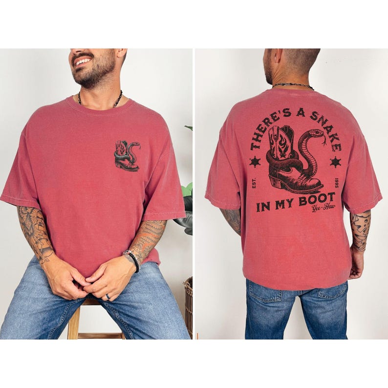 May include: A red t-shirt with a graphic of a snake coiled around a cowboy boot. The front of the shirt has a smaller version of the graphic. The back of the shirt has the text "THERE'S A SNAKE IN MY BOOT" with stars and the words "Yee-Haw".
