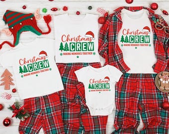 May include: A festive collection of Christmas pyjamas and accessories. White tops and a baby onesie display the text "Christmas Crew" with a Santa hat and Christmas tree. The plaid trousers are red and green. Ornaments and a hat are also included.
