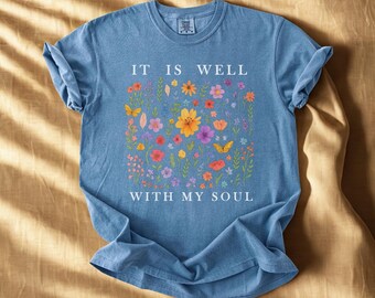 May include: A blue t-shirt with the words "IT IS WELL WITH MY SOUL" in white. The shirt features a floral design with yellow, orange, pink, and purple flowers, and yellow butterflies.