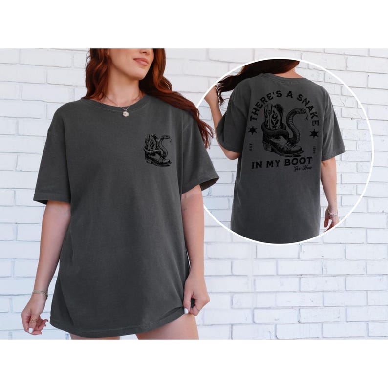 May include: Dark grey t-shirt with a black graphic of a snake coiled around a boot on the front and back. The back of the shirt has the text "THERE'S A SNAKE IN MY BOOT" with star accents. The shirt is a casual, unisex style.