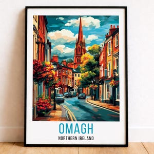 Puede incluir: Una impresión enmarcada de acuarela de Omagh, Irlanda del Norte, que muestra una escena callejera con edificios coloridos, un campanario y coches. El cielo es azul con nubes blancas. El texto "OMAGH" y "NORTHERN IRELAND" están en la parte inferior.