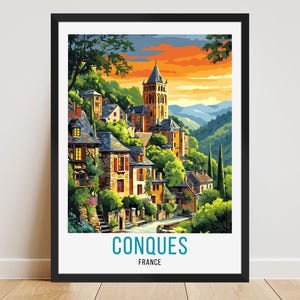 May include: A framed art print featuring a colorful illustration of Conques, France. The artwork depicts a village nestled on a hillside with a church tower, surrounded by lush greenery and a vibrant sunset sky. The text "CONQUES FRANCE" is at the bottom.