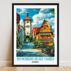 Könnte beinhalten: Ein gerahmter Kunstdruck von Rothenburg ob der Tauber, Deutschland. Das Bild zeigt eine farbenfrohe Straßenszene mit einem Turm, Gebäuden und einem blauen Himmel mit Wolken. Der Text "ROTHENBURG OB DER TAUBER GERMANY" steht unten.