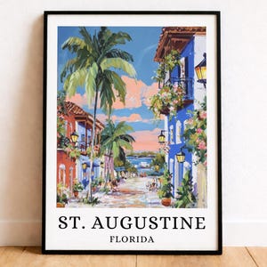 Peut inclure: Une impression d'art encadrée représentant une scène de rue à St. Augustine, en Floride. L'illustration montre des bâtiments colorés, des palmiers et des fleurs suspendues sous un ciel bleu. Le texte ST. AUGUSTINE FLORIDA est imprimé en noir.