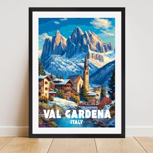May include: A framed art print of Val Gardena, Italy, featuring a snow-capped mountain range under a blue sky. The artwork depicts a village with buildings, a church, and the text "VAL GARDENA ITALY".