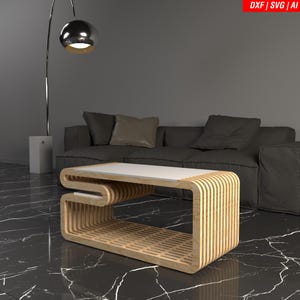 May include: A modern wooden coffee table with a white top and a unique, curved design. The table is made of light-colored wood and features a slatted base. The image also includes a dark gray sofa, a floor lamp, and the text "DXF | SVG | AI".