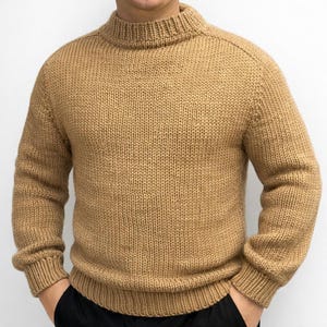 Pode incluir: Um suéter de malha bege com gola alta canelada. O suéter tem uma malha grossa e mangas compridas. A peça de roupa é de cor lisa e parece ser feita de um material quente, possivelmente lã.